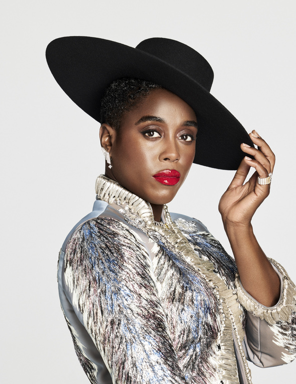 Elegant Black woman in a wide-brimmed black hat and patterned coat with red lipstick posing in front of a white background.