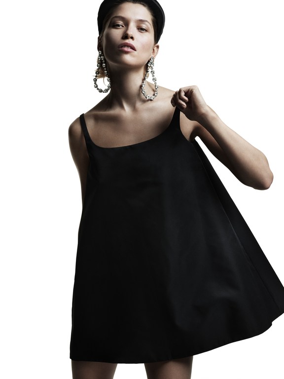 Model in black minidress wearing large crystal earrings and headband against a bright white background
