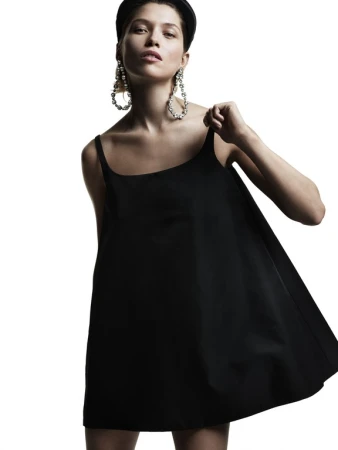 Model in black minidress wearing large crystal earrings and headband against a bright white background