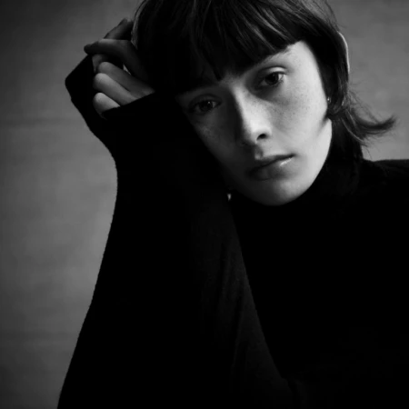 Close-up portrait of a woman with dark hair and bangs wearing a black turtleneck sweater, photographed in monochrome.