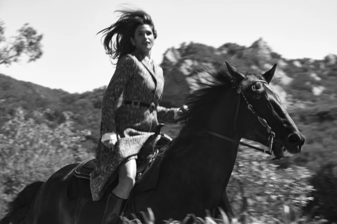 Black and white photograph of a woman riding a dark horse through a landscape, hair blowing in the wind.