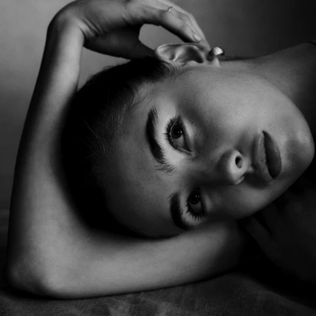 Close-up monochrome portrait of a woman lying down with her hand resting behind her head, photographed by Victor Demarchelier.