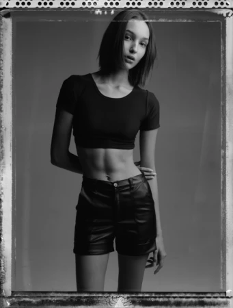 Black and white portrait of a woman with short hair wearing a black crop top and leather shorts in a studio.
