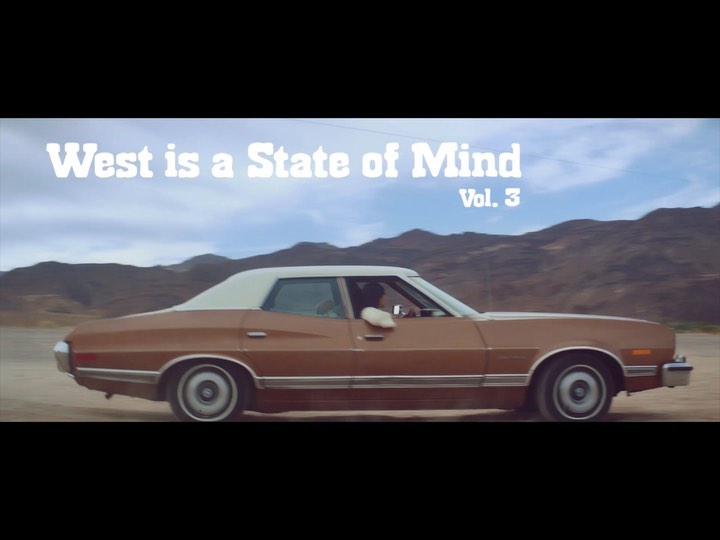 Vintage brown car driving through a desert landscape with mountain backdrop, showcasing a nostalgic and scenic automotive scene.