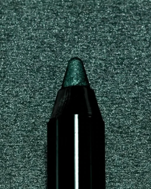 Close-up of a dark green eyeliner pencil with a shiny tip, set against a dark glittering green background.
