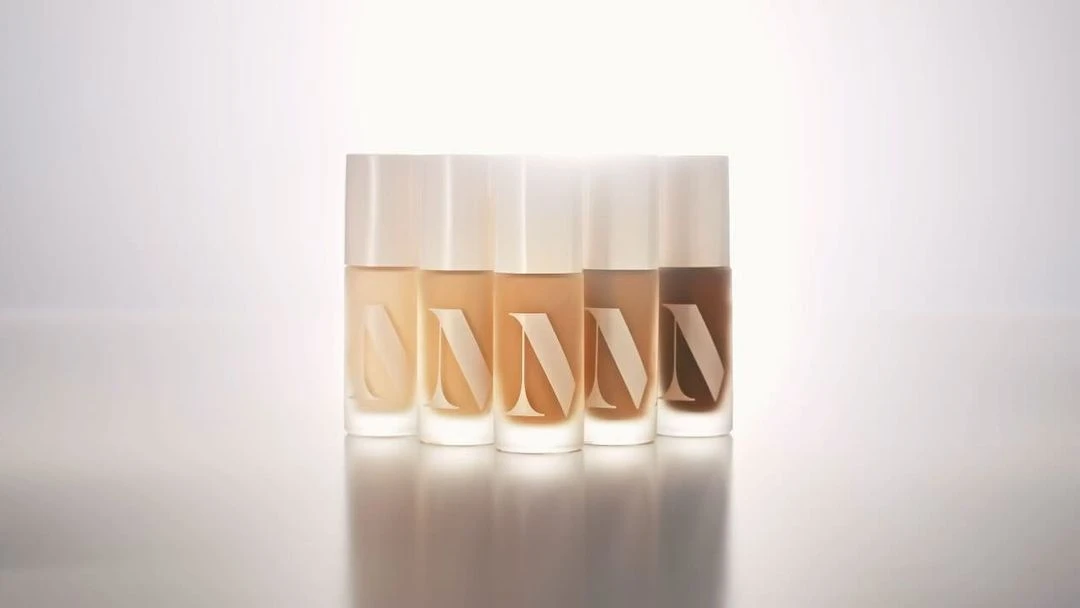 Five bottles of diverse-toned foundation arranged closely, showcasing a range of skin tones on a reflective surface, beauty concept.