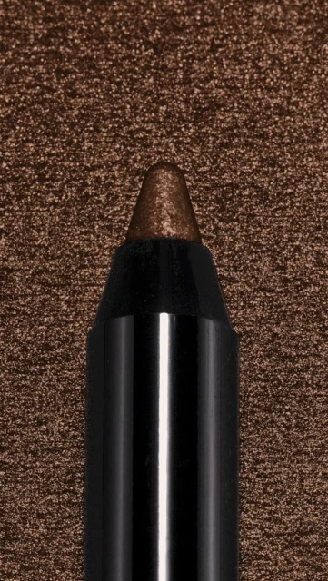 Close-up of a brown eyeliner pencil with a black casing, positioned against a textured brown background. Beauty product detail.