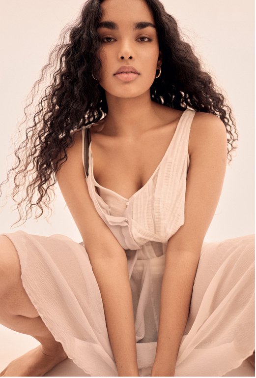 Brunette woman with curly hair poses in a light pink outfit in a close-up studio shot for fashion, beauty, and lifestyle advertising.