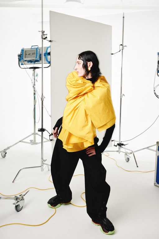 Stylish person in yellow top poses in a photo studio with lighting equipment and backdrop. Fashion editorial photography with a modern aesthetic.