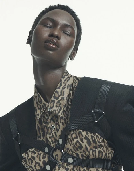 Close-up studio portrait of an adult female model with dark skin wearing an animal print shirt and black blazer with harness straps. 