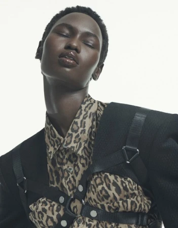 Close-up studio portrait of an adult female model with dark skin wearing an animal print shirt and black blazer with harness straps. 