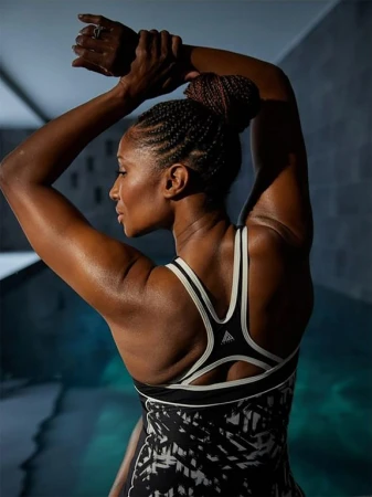 Athletic woman in activewear poses in an indoor environment with a pool, showcasing fitness and style with her braided updo hairstyle.