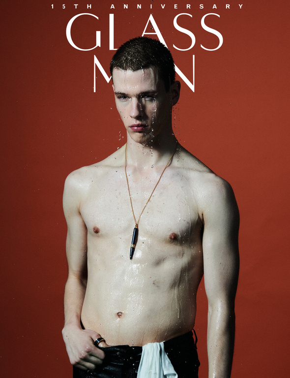 Shirtless young man with wet hair wearing a gold pendant necklace against a deep red background for Glass Man magazine editorial