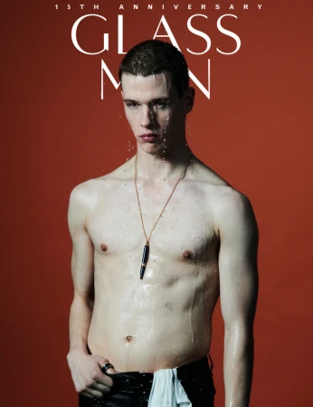 Shirtless young man with wet hair wearing a gold pendant necklace against a deep red background for Glass Man magazine editorial
