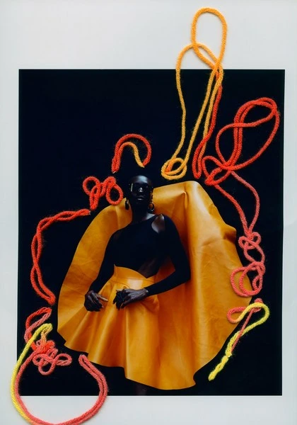 Fashion editorial shot with model in yellow skirt and top against black background with coral and yellow yarn detail