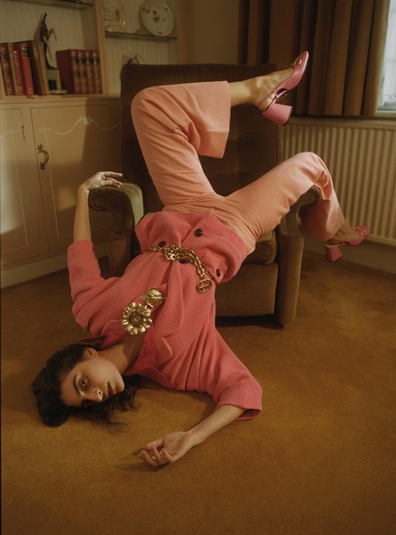 Woman in pink suit poses upside down on a chair in an indoor setting; fashion, style, and creative photography.