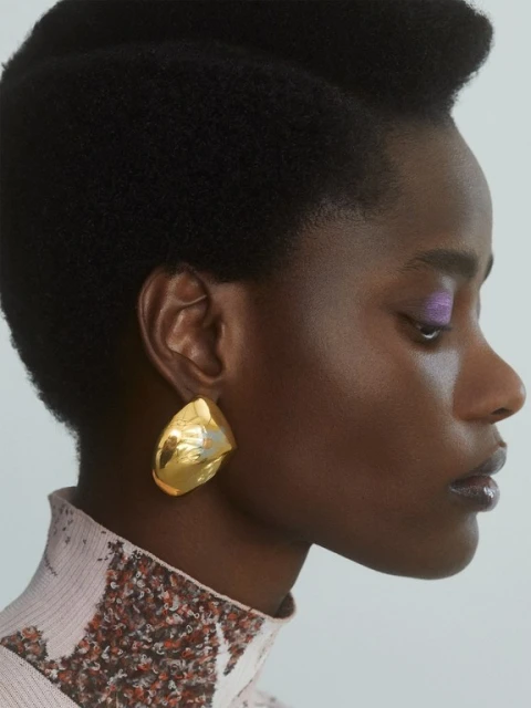 Close-up of a stylish African-American woman with a golden earring, light purple eyeshadow, and a high-necked textured top.