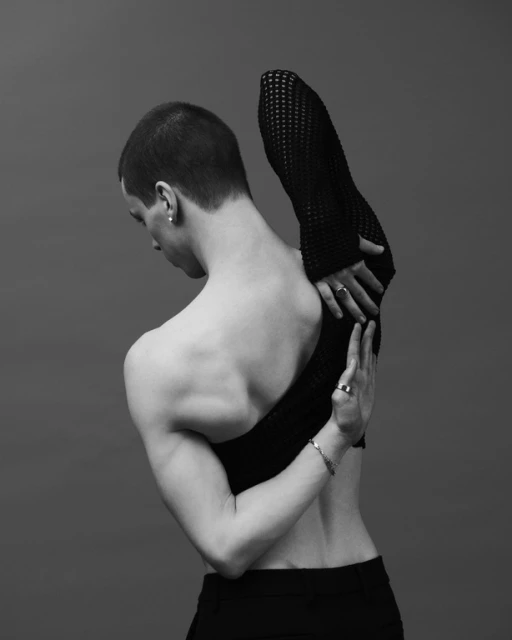 Black and white portrait of a muscular adult male in a studio. The man has short hair, rings, and a bracelet. He is wearing black clothing.