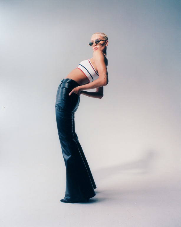 Fashionable adult woman with short blonde hair posing in a crop top and black flared pants in a studio setting with soft lighting.