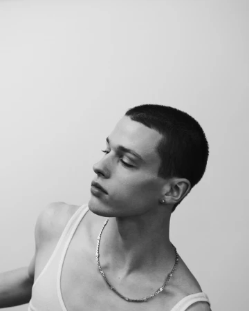 Portrait of a man wearing a white tank top and silver chain necklace against a light background