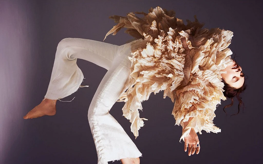Fashion shot featuring a person in a white outfit with a textured, paper-like top against a gradient grey background, studio lighting, stylish and unique.