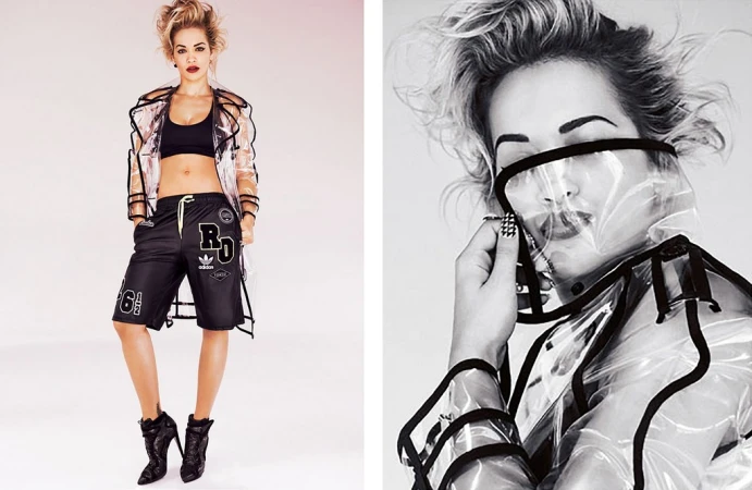 Model poses in a clear jacket, black bra top, and Adidas shorts against a white background in a studio fashion shot.