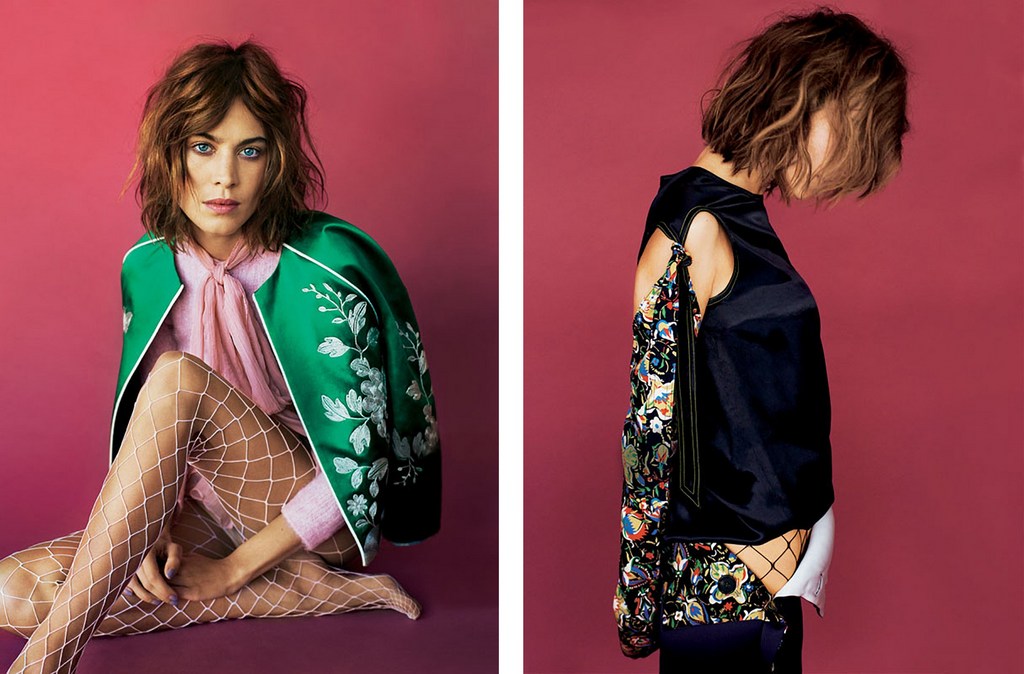 Fashion shot of a woman with bob haircut in a green floral jacket, pink top and white fishnet stockings, posing in a photo studio with pink backdrop.