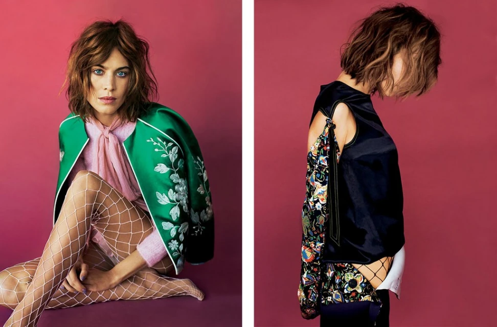 Fashion shot of a woman with bob haircut in a green floral jacket, pink top and white fishnet stockings, posing in a photo studio with pink backdrop.