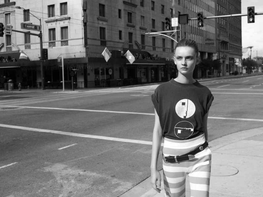 Monochrome fashion shot of a woman standing on a crosswalk in a city, wearing a t-shirt with a graphic and striped pants.