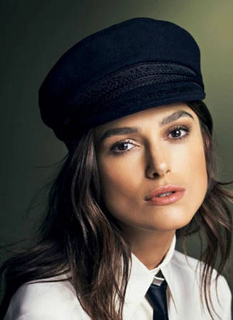 Portrait of Keira Knightley wearing a dark navy cap and white collared shirt styled by Natalie Hartley.