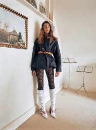 Model in dark jacket, patterned leggings and white boots posing in a light room styled by Natalie Hartley