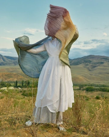 Model in a white dress holding a flowing gradient scarf outdoors in a hilly landscape styled by Tess Yopp