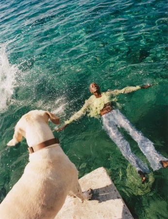 Woman in water with dog. Woman in sheer top and silver pants floating in clear water, dog on concrete pier looking at her.