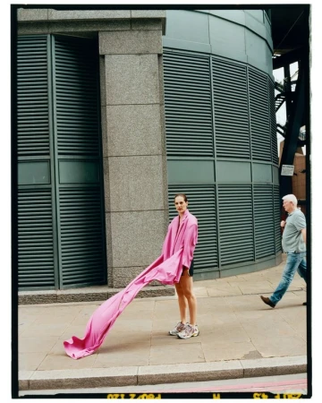 Model standing on a London sidewalk holding a flowing pink garment, with a second person walking past.