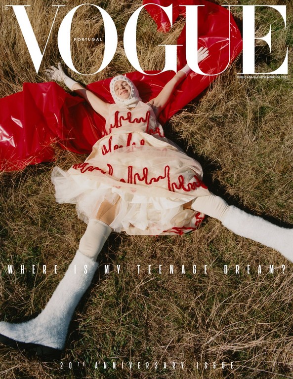 Vogue Portugal cover featuring a model in a white and red dress lying on grass, with a red plastic cape and white thigh-high boots.