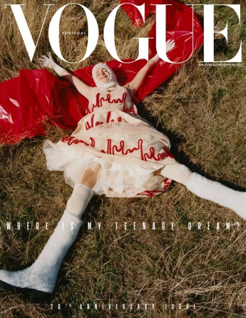 Vogue Portugal cover featuring a model in a white and red dress lying on grass, with a red plastic cape and white thigh-high boots.