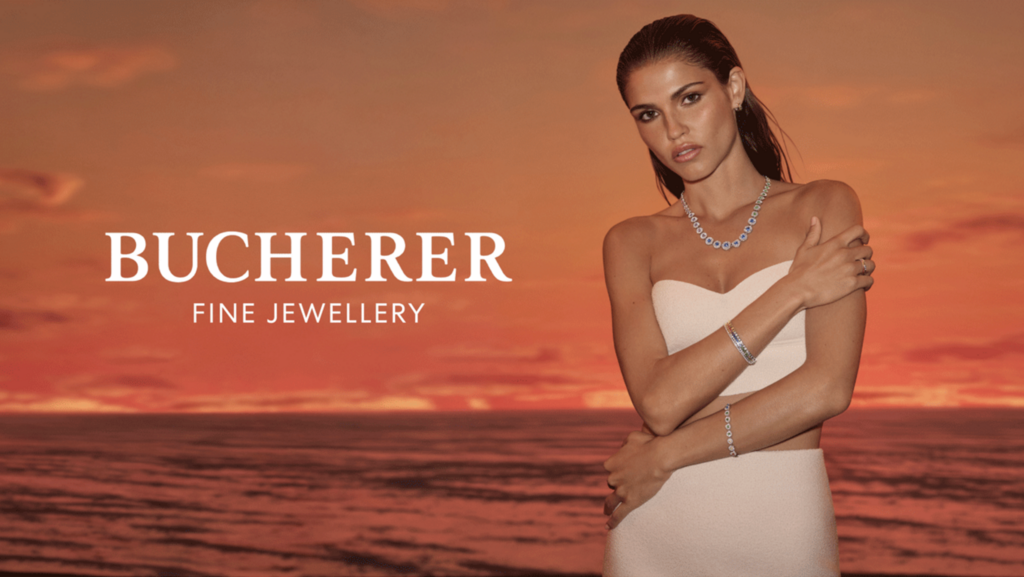 A tanned woman poses in a strapless dress with Bucherer Fine Jewellery, set against a dramatic orange sunset and rippling ocean.