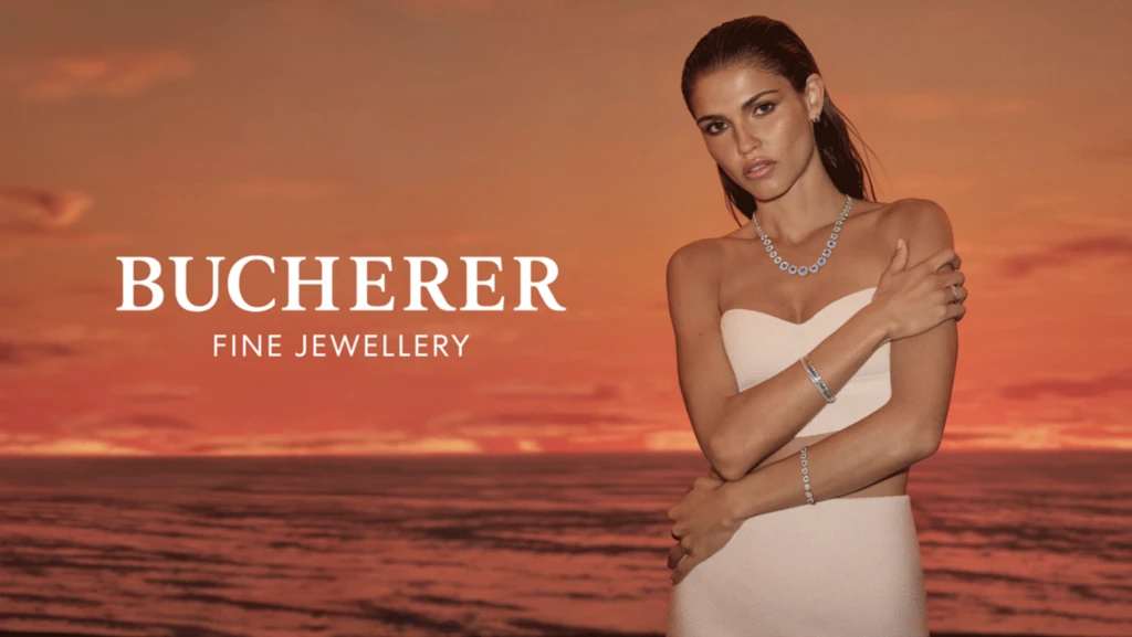 A tanned woman poses in a strapless dress with Bucherer Fine Jewellery, set against a dramatic orange sunset and rippling ocean.