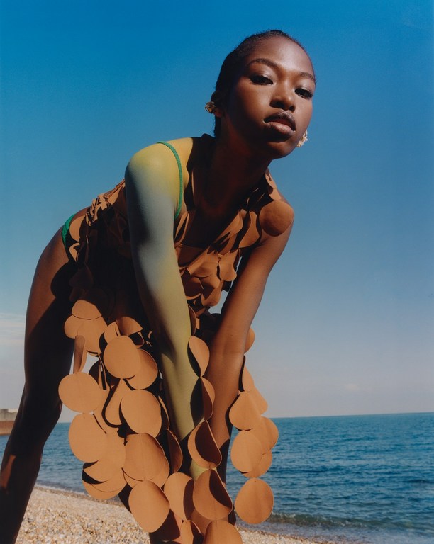 Fashionable young woman poses on a beach wearing a modern, earth-toned disc dress with the ocean and blue sky in the background.