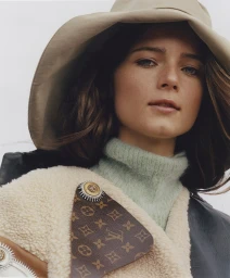 Close-up portrait of a woman wearing a wide-brimmed tan hat and a monogrammed leather jacket styled by Tess Yopp.