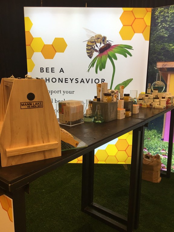 Close up of a display with honey and honey products at a trade show, featuring a large bee graphic and beekeeping equipment.