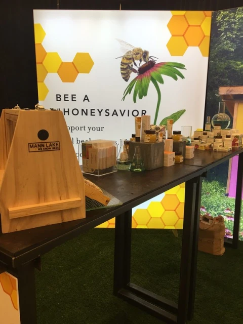 Close up of a display with honey and honey products at a trade show, featuring a large bee graphic and beekeeping equipment.