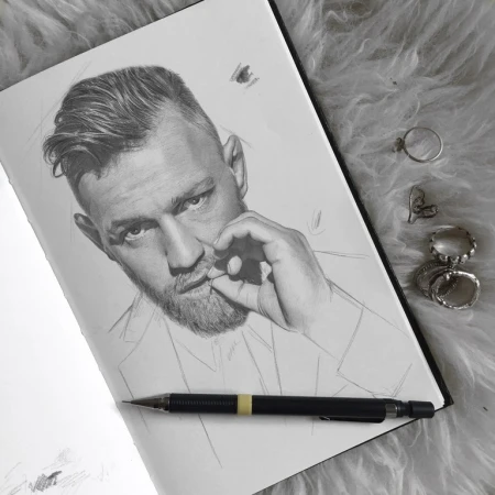 Pencil drawing of fair-skinned adult male with beard, sketched in profile on notebook paper, with pencil and rings on furry surface.