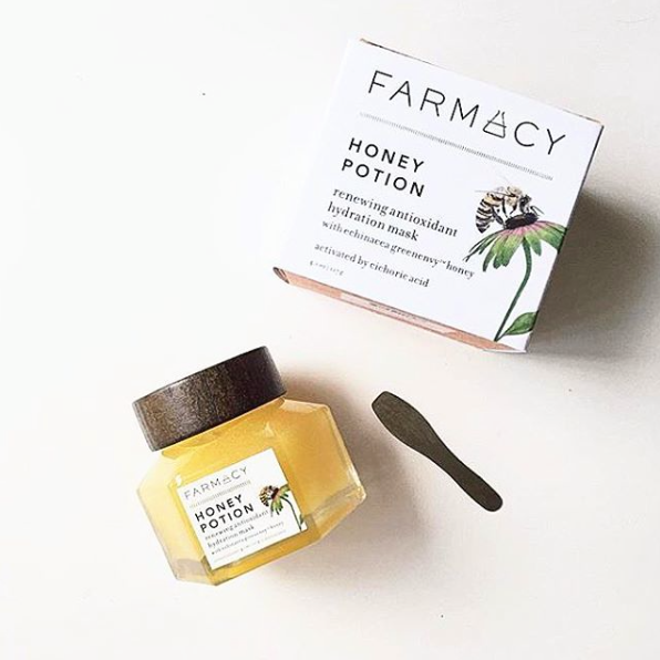 Two skincare products: a jar of Farmacy Honey Potion antioxidant hydration mask and the product box, next to a small spatula on a white surface.