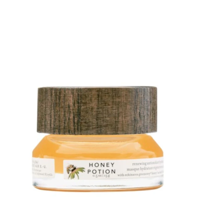 Close-up of a small, clear glass jar filled with honey potion, featuring a wooden lid and labels with text and floral designs.