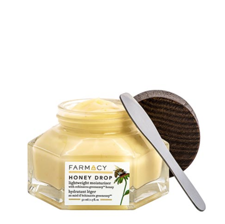 Close-up of Farmacy Honey Drop moisturizer in a clear jar with a wooden lid and spatula, set against a clean white background.