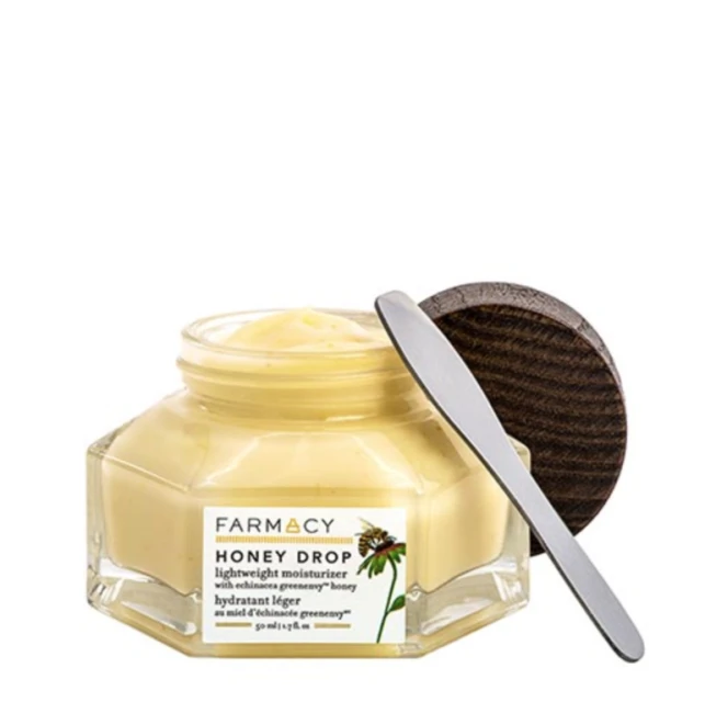 Close-up of Farmacy Honey Drop moisturizer in a clear jar with a wooden lid and spatula, set against a clean white background.