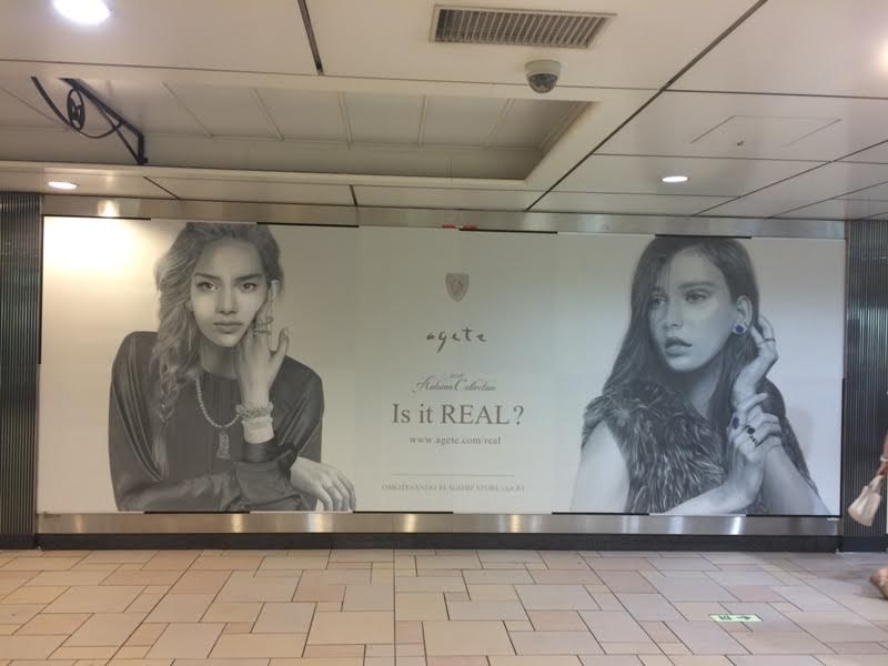 Advertising billboard in an underground transit station featuring two women wearing jewelry, promoting the brand agete, in black and white.