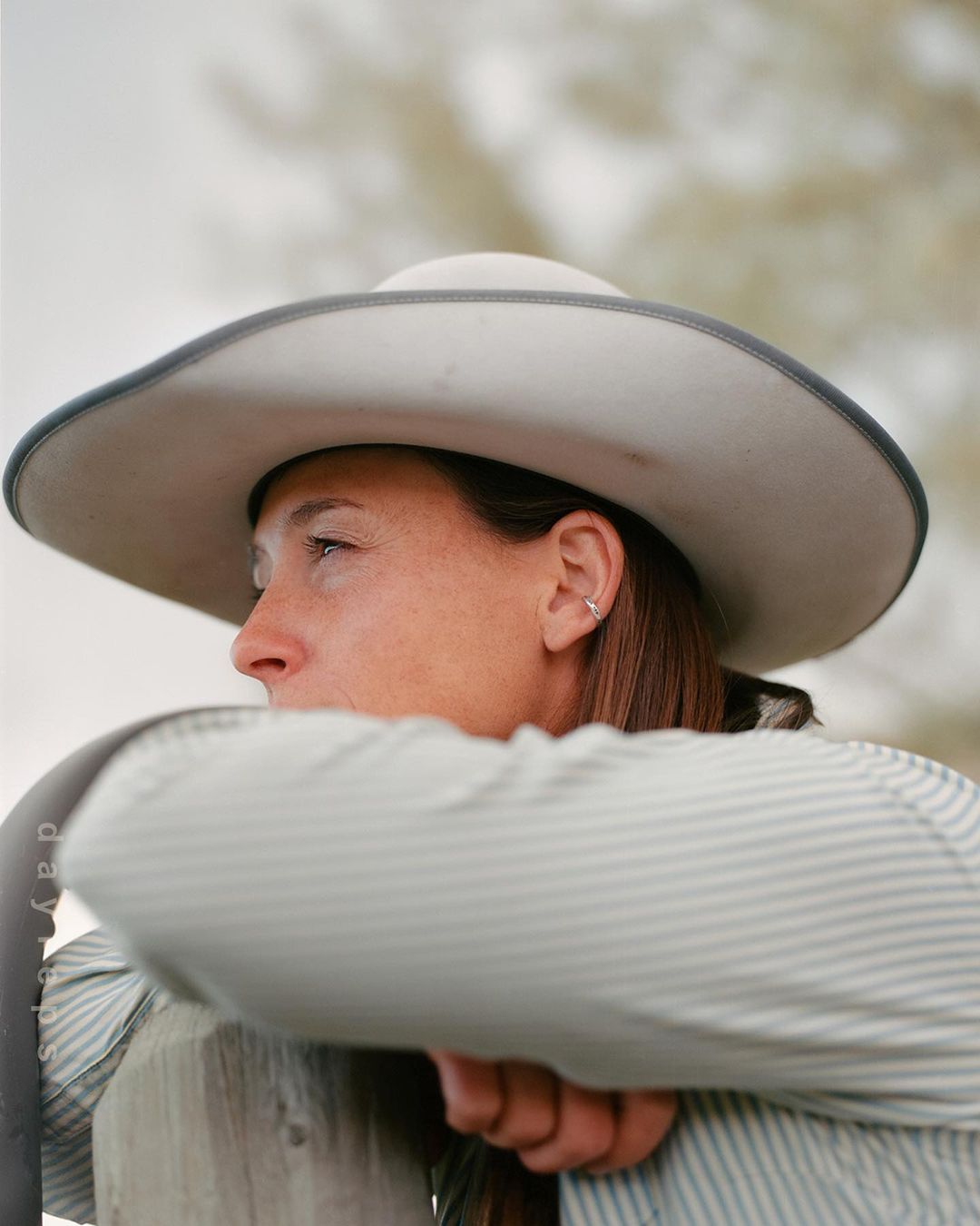 Woman with cowboy hat outdoors in natural light. Profile view of person in hat and striped shirt looking left. Neutral background.