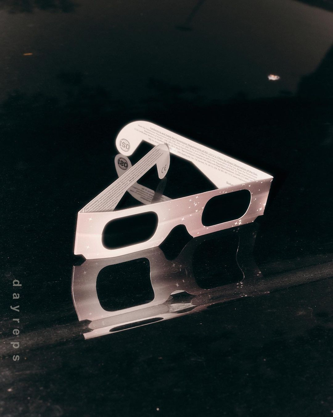 Close-up of eclipse glasses with reflective surface, featuring light and dark contrasts, with text 'dayreps' visible along the side.